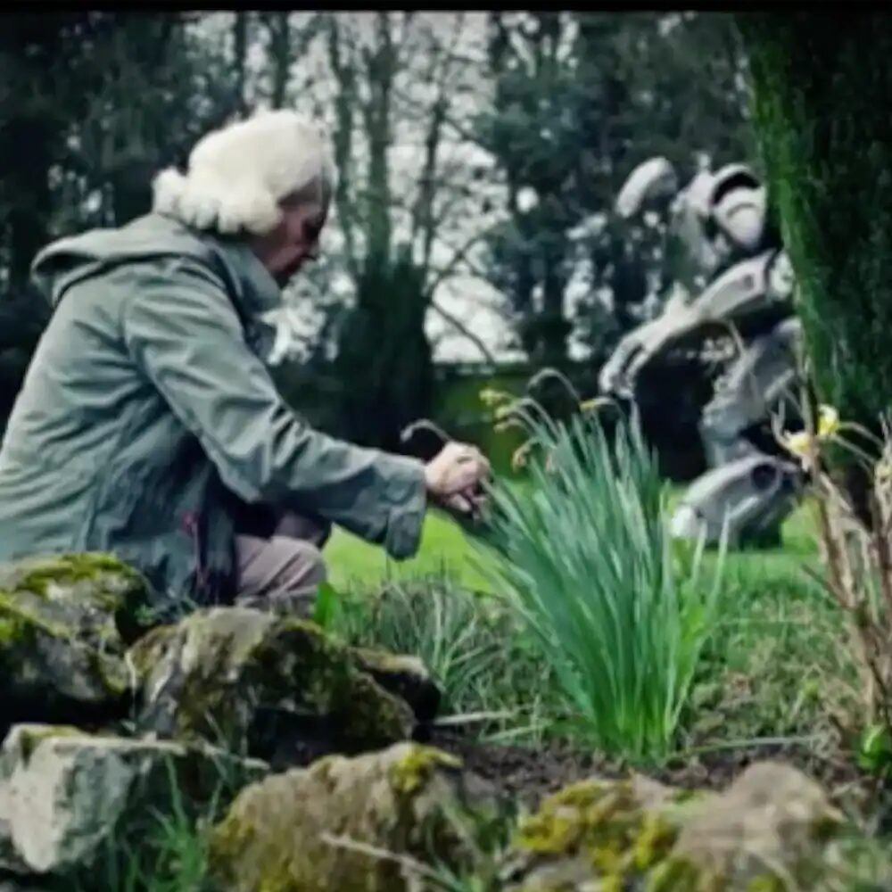 An old woman gardening, with Titan the Robot in the background pushing a lawnmower.