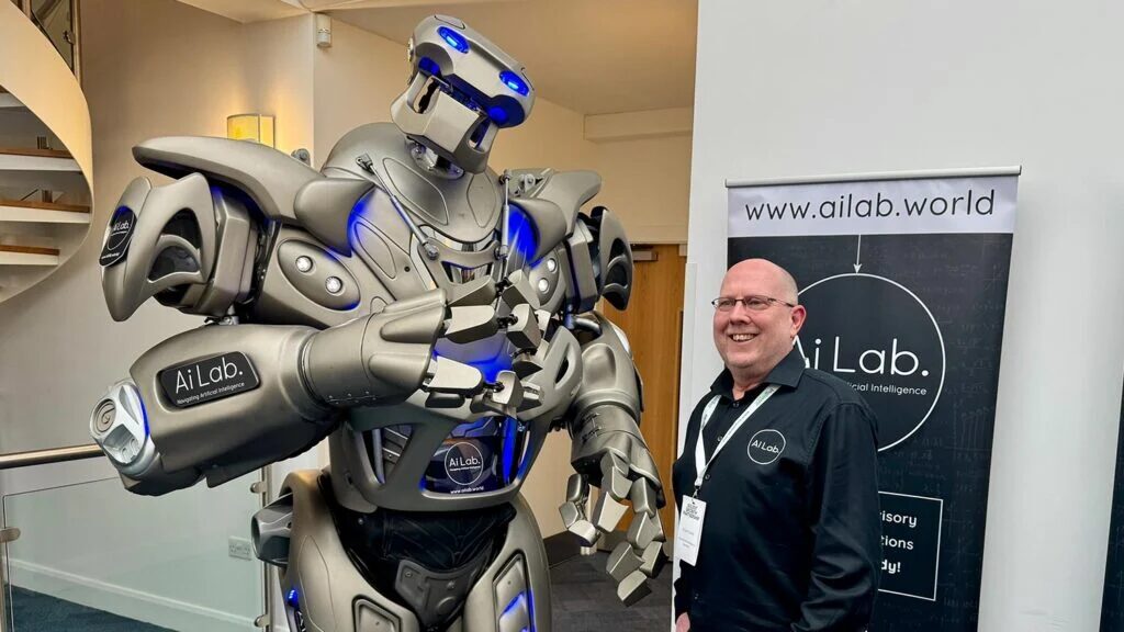 Titan the Robot stands next to the owner of AI Labs, with AI Labs branding panels on display.